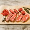 flatlay of multiple slices of steak on parchment paper with thyme and garlic cloves